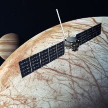 A conception of the Europa Clipper spacecraft flying over Jupiter's moon Europa.