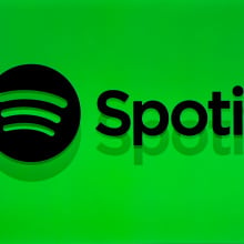 The silhouette of a person wearing headphones in front of the Spotify logo and name on a bright green background.