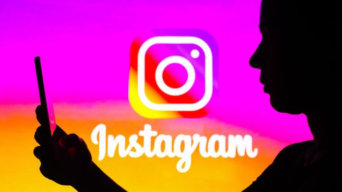  Woman's silhouette is holding a smartphone with an Instagram logo in the background. 