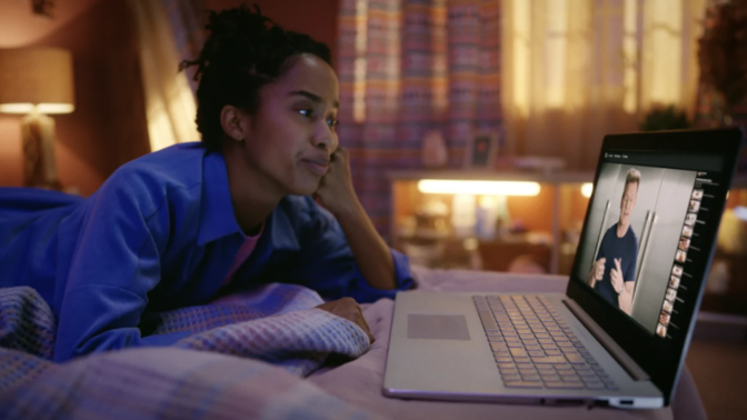 Person laying on bed watching MasterClass on laptop