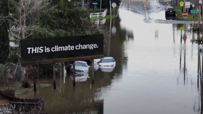 A billboard rises above a flooded street. It reads, "This is climate change."