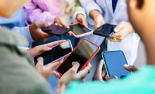 Young group of people standing in circle using mobile phones outside. Unrecognizable teen friends watching social media content on smartphone app. 