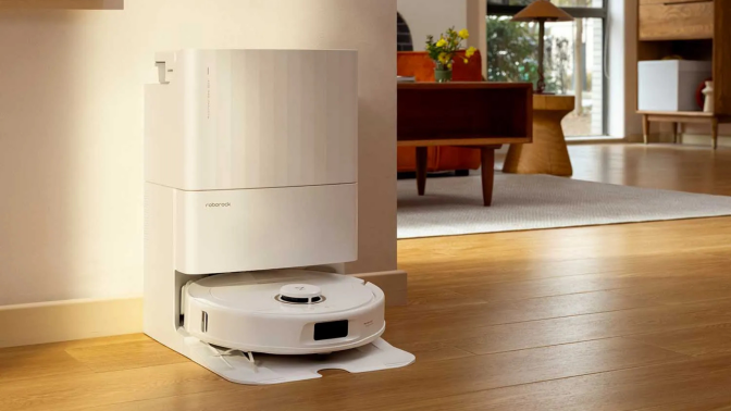 White Roborock vacuum and dock sitting against wall with living room furniture in background