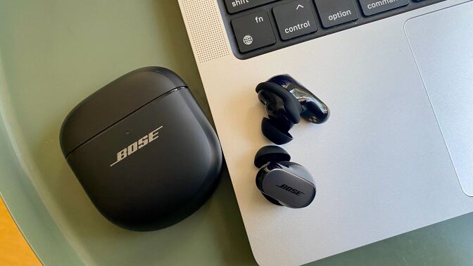 bose quietcomfort ultra earbuds on table next to macbook