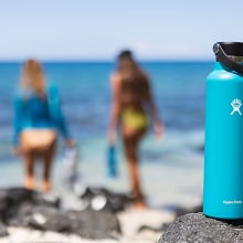 Blue water bottle on rocks wit two people on beach walking away out of focus in background