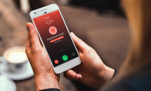 a woman holding an iphone receiving a call that's flagged as spam by the truecaller app