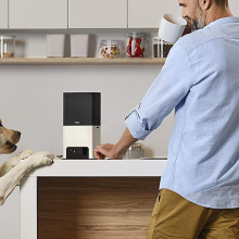 man standing beside dog and treat tossing camera