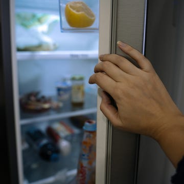 female hand close up opening a fridge door with food at home