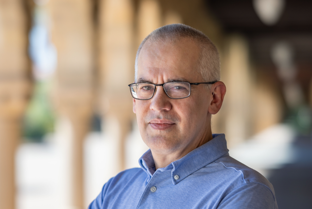 Matthew Sommer wearing a light-blue collared shirt standing under one of arcades on Stanford's Main Quad