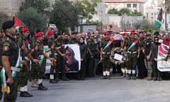 Palestinian security forces line a road as colleagues carry Ayşenur Ezgi Eygi's covered body on a stretcher at shoulder height surrounded by mourners