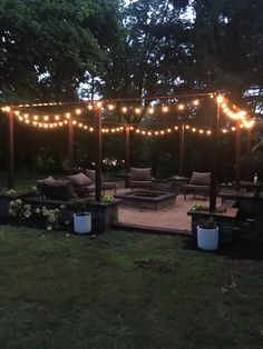 an outdoor patio with lights strung over the fire pit and seating area for people to sit on