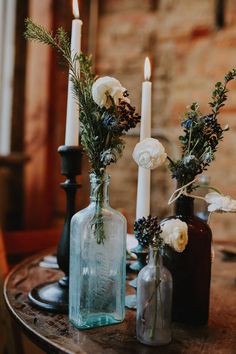 three vases with flowers are sitting on a table in front of two white candles