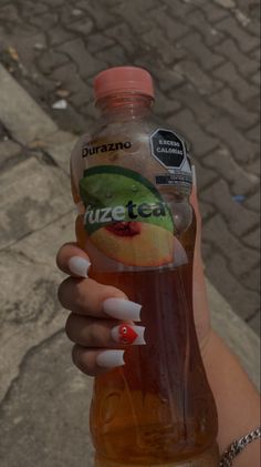 a person holding up a bottle of juice with fruit on the top and white nails