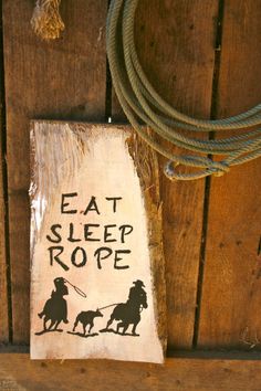 a sign that says eat sleep rope on the side of a wooden wall next to a rope