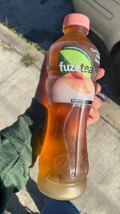 a person holding a bottle of fruit tea in their left hand on the sidewalk next to a car