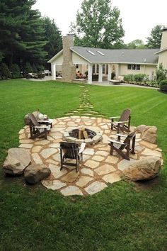 a stone fire pit in the middle of a lawn with chairs around it and a house in the background