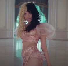 a woman with long hair wearing a pink outfit and posing for the camera in a white room