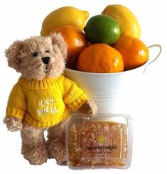 a teddy bear wearing a sweater next to a bowl of oranges and lemons