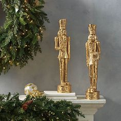 two gold figurines sitting on top of a mantle next to a christmas wreath