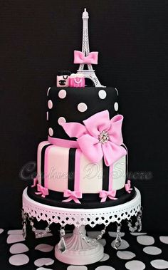 a three tiered cake decorated with pink and black polka dots, the eiffel tower is in the background