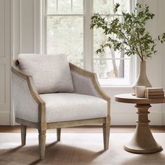 a white chair sitting next to a vase with a plant in it on top of a table