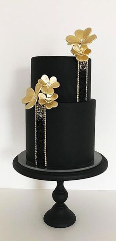 a black and gold wedding cake with flowers on top