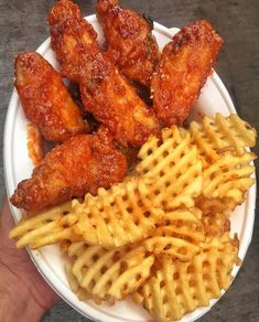 chicken wings, waffle fries and macaroni salad on a white plate with someone's hand