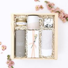 an open box with some items in it and pink flowers on the table next to it