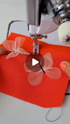 someone is using a sewing machine to sew flowers on an orange piece of fabric