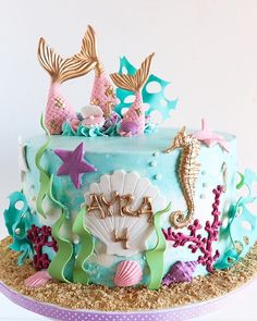 there is a blue cake decorated with mermaids and seashells on the top