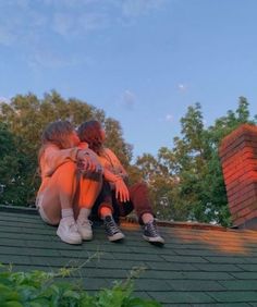 two people sitting on the roof of a house with their arms around each other as they hug