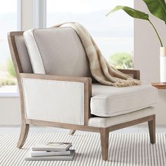 a chair with a blanket on top of it in front of a window and a potted plant