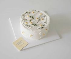 a white cake with daisies on it sitting on top of a piece of paper