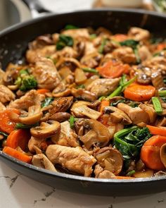 a skillet filled with chicken, mushrooms and broccoli on top of a table