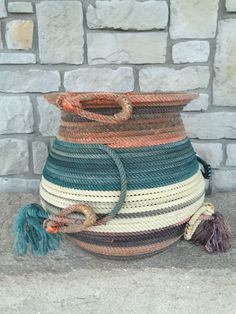 a multicolored basket sitting on the ground next to a brick wall with a tassel hanging from it