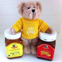 a brown teddy bear wearing a yellow sweater and two jars of honey