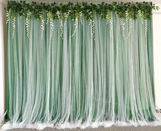 a green curtain with white flowers and greenery hanging from it's sides in front of a wall