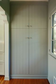 an empty room with wooden floors and white cabinets on the wall, next to a window