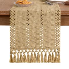 a table runner with tassels on it and plates of food in the background