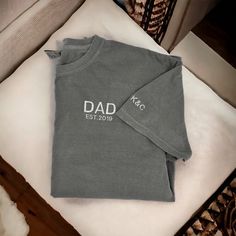 "These embroidered Dad T-shirts make a great Father's Day gift! Customized with the year they became a dad and the kids initials on the sleeve! **If you would like this shirt customized beyond adding the est. year and initials on the sleeve, please email us first to make sure that the changes are possible. There will be a $10 charge for extra customization outside of est. year and initials. We will then let you know to pick the \"extra customization\" option in the color selection in the size you need. When doing this please put the color shirt you would like from the available options in the personalization box along with your other customizations.**  ORDERING & SHIPPING *Your item will be shipped within 5-7 business days. *Please allow 2-5 business days to receive your item, more time ma Dad Established Shirt, Dad Shirts Father's Day, Dad Tshirt Ideas, Fathers Day Embroidery, Dad Aesthetic, Dad Tshirt, Papa T Shirt, T-shirt Broderie, Papa Shirts