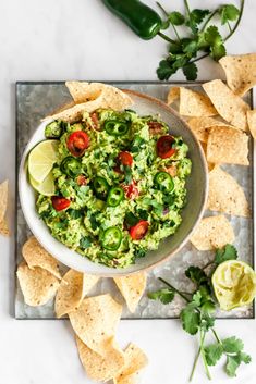 a bowl filled with guacamole surrounded by tortilla chips and cilantro