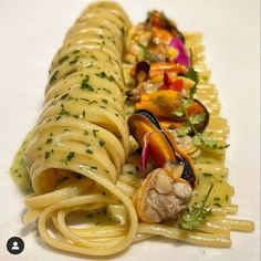 two pastas with sauce and vegetables are on a white tablecloth, one is cut in half