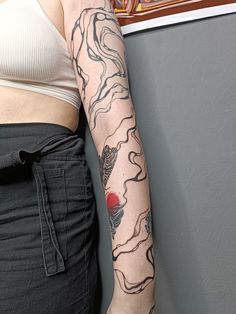 a woman with a tattoo on her arm is standing next to a wall and looking at the camera