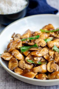 a white bowl filled with mushrooms and green onions next to rice on a blue table cloth