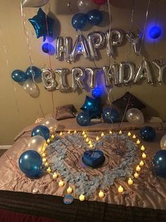 a birthday cake with candles and balloons in the shape of a heart on a bed