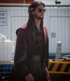 a man with long hair and sunglasses standing in front of a fenced off area