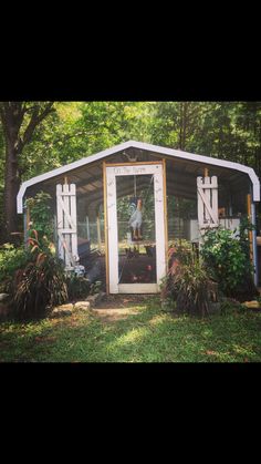 a chicken coop in the middle of some trees and bushes with a person on it