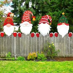 three christmas gnomes sitting on top of a wooden fence