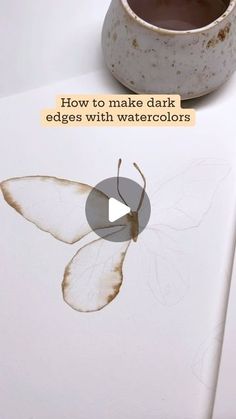 a white vase sitting on top of a table next to a piece of paper with a butterfly drawn on it