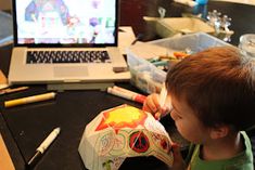 a young boy is eating something in front of a laptop computer on a desk with markers and pencils